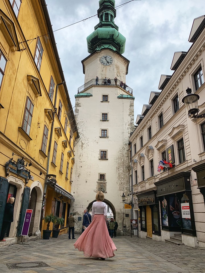 Caucasian woman with pint swirl skirt looking at white tower