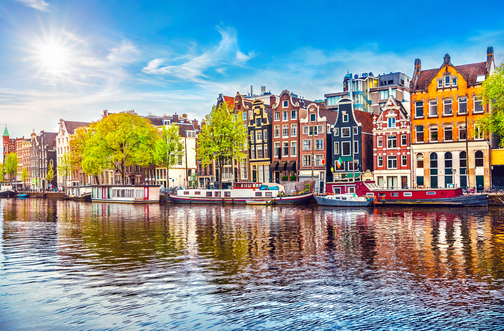 Colorful canal houses and house boats along the water on a sunny day in Amsterdam.