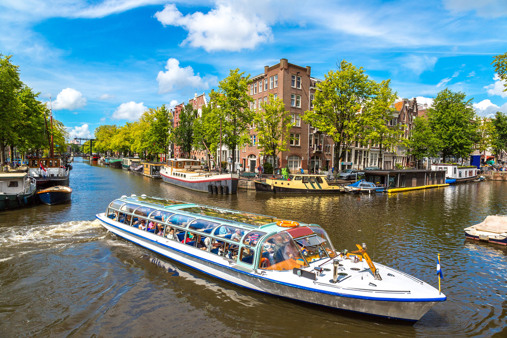 A glass roofed boat cruising down a canal during 1 day in Amsterdam.