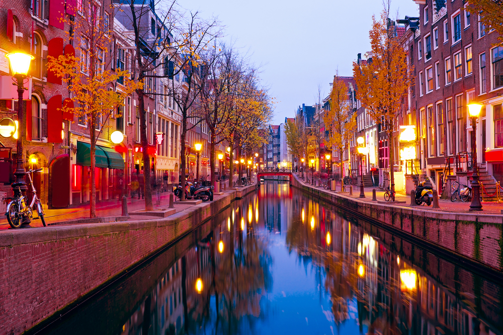 Dusk over a canal running through the red light district with lights reflected in the water.