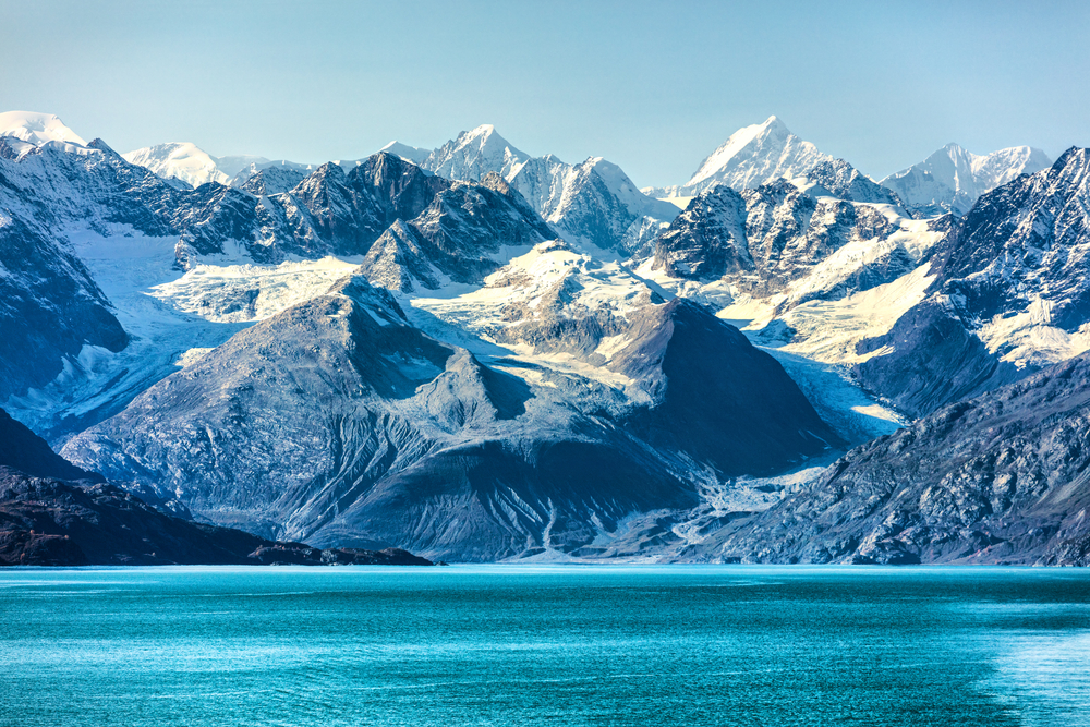 Mountains covered with glaciers and snow with bright blue water in foreground.