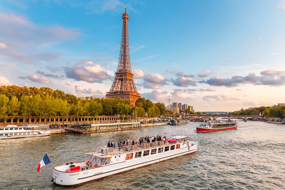 Cruise boats passing the Eiffel Tower on the Seine River at sunset.