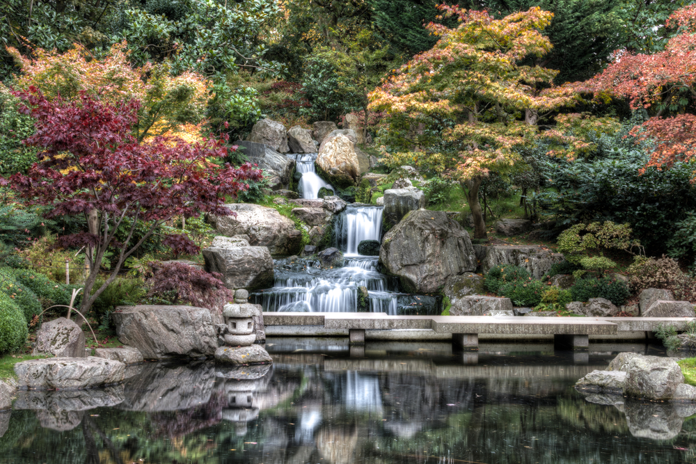 A waterfall cascading into a pond in Kyoto Gardens with fall foliage.