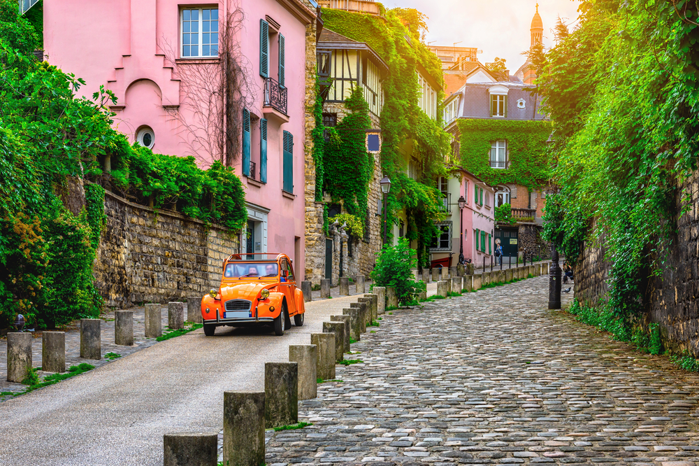 View of old street in quarter Montmartre in Paris, France. Cozy cityscape of Paris. You can see a pink building and an orange car. 