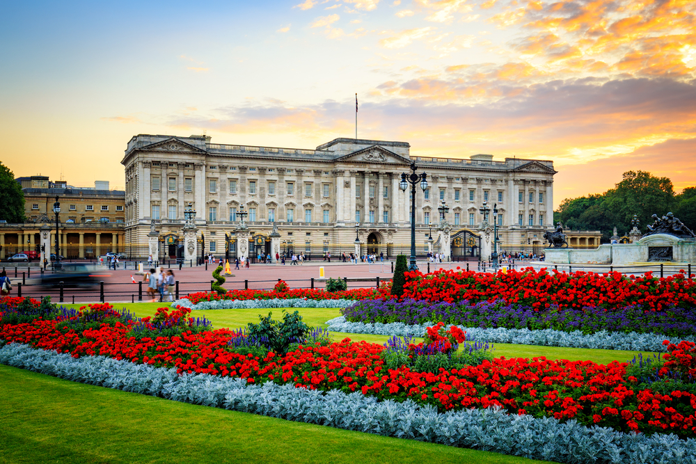 Buckingham Palace at sunset with brightly colored flower beds in the foreground.