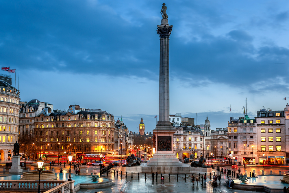 Trafalgar Square at dusk with fountains and a large column with a statue in the center.