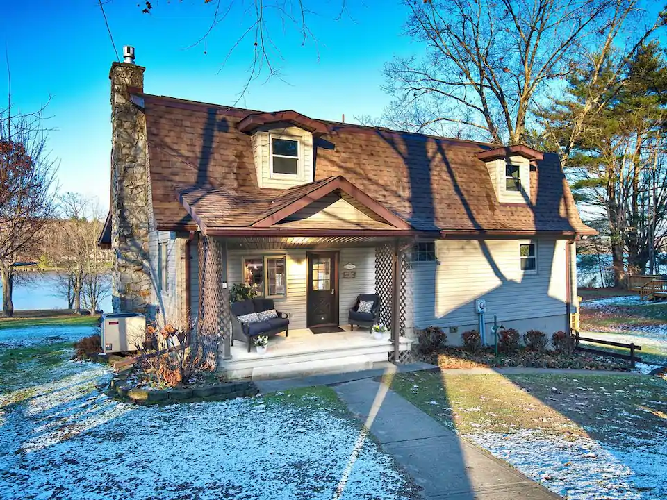 Charming house on a lake with dusting of snow on its front lawn.