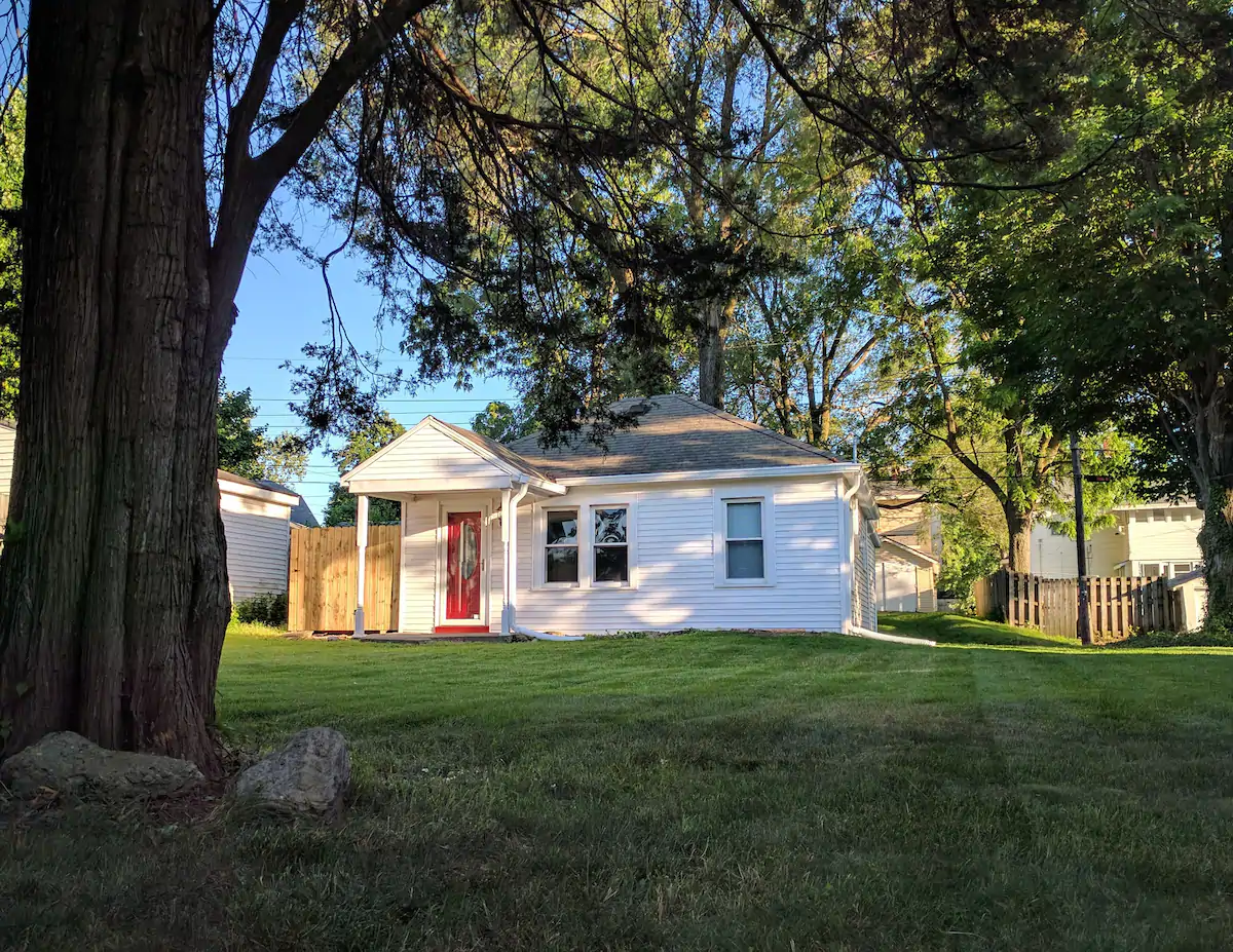 Charming cozy white house in large yard with red front door.