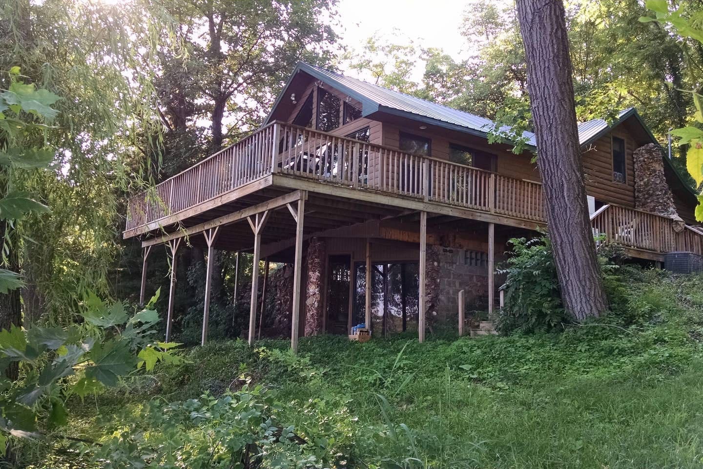 Brown wooden treehouse with wraparound balcony with wooden fence surrounded by green trees. Wisconsin Airbnbs