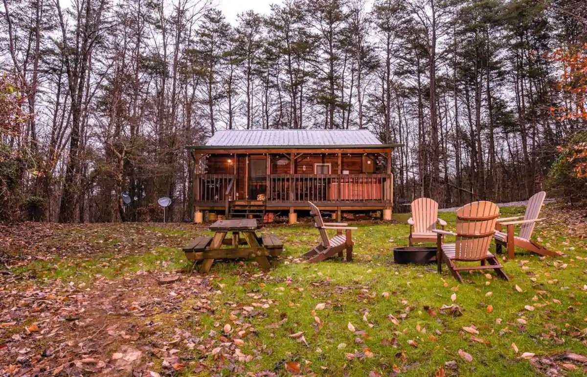 Cozy studio cabin with wooden lawn chairs and picnic table in yard