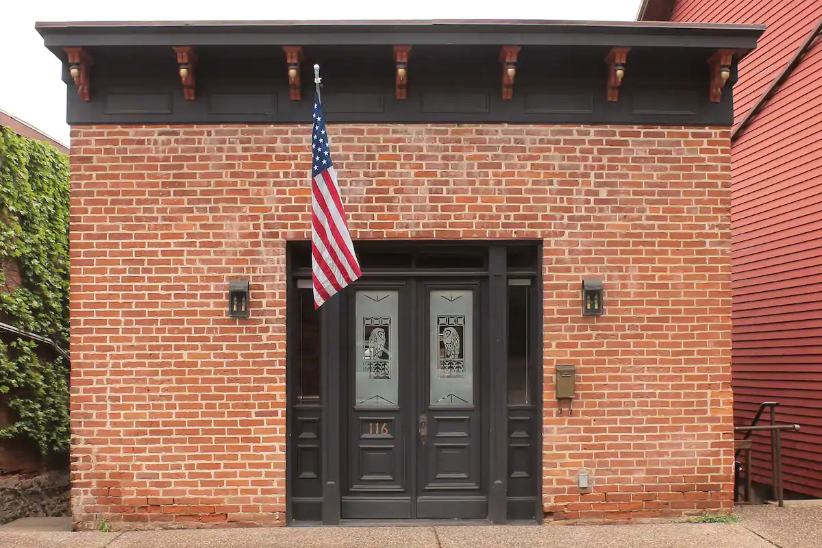 Photo of red brick building with American flag flying and owl etchings on the windows of the front doors.