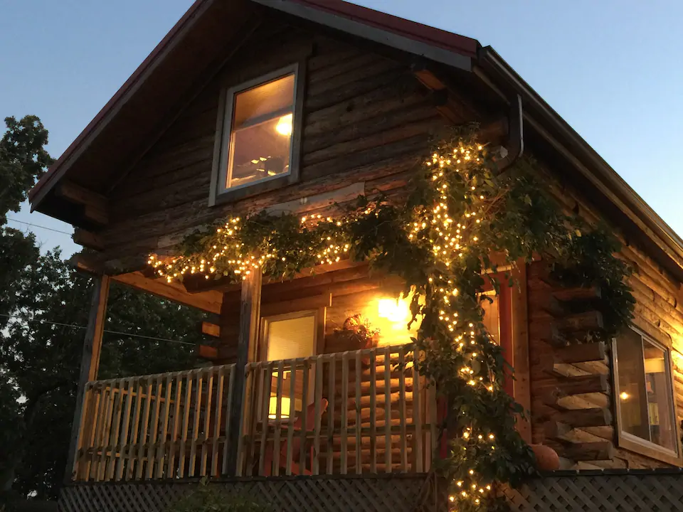 Photo at dusk of rustic 2 story cabin with lovely porch and lights on trees