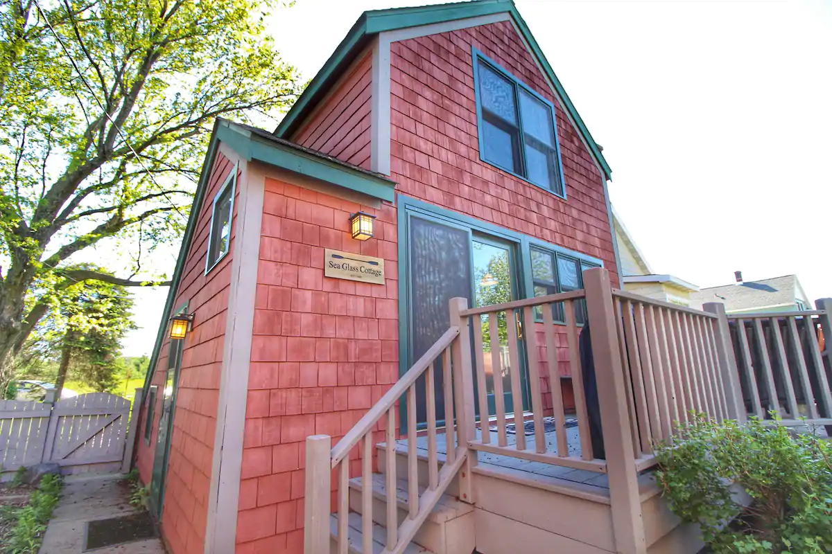 Red cottage with steps leading up to front patio. Green trim on the roof makes it a cute Airbnb in Duluth.