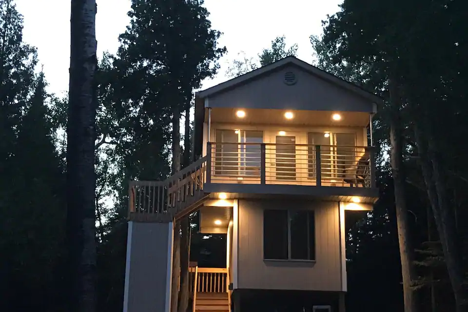 Cute treehouse-style Minnesota cabin at sunset illuminated with bright lights.