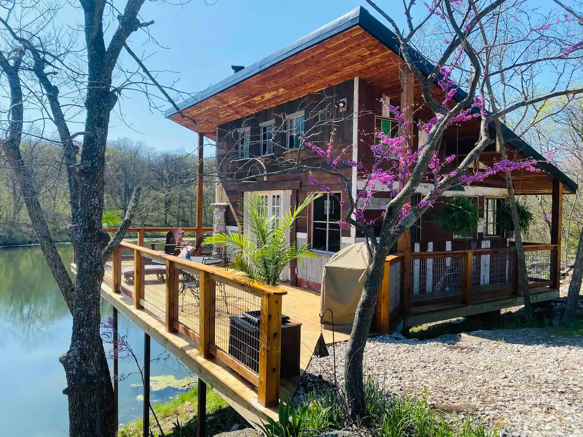 Cabin sitting on deck over lake with slanted roof in bright sunny day making this one of the best cabin rentals in Missouri