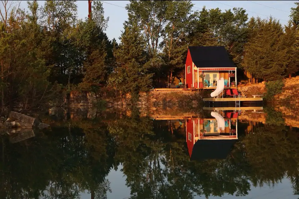Bright red tiny house with patio and a white slide in beautiful setting on water.