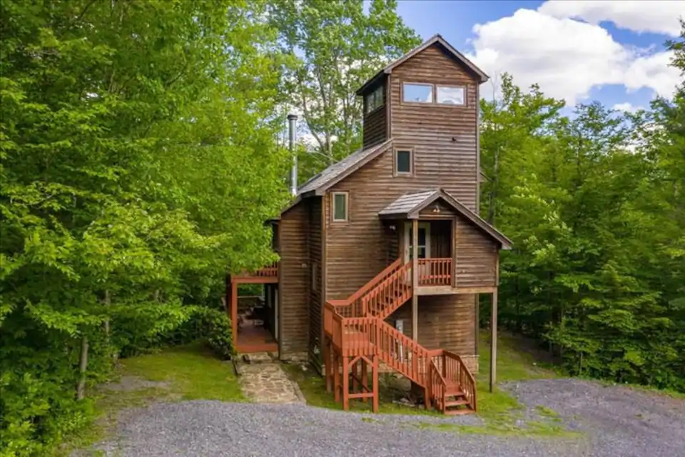 Picture of tall and large cabin set among forested trees with beautiful wooden staircase. Airbnbs in West Virginia