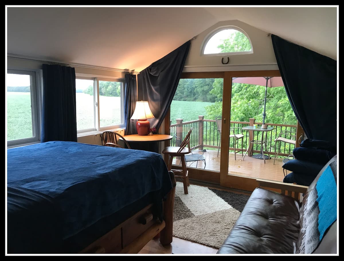 Photo of bedroom with glass windows and balcony showcasing the countryside.