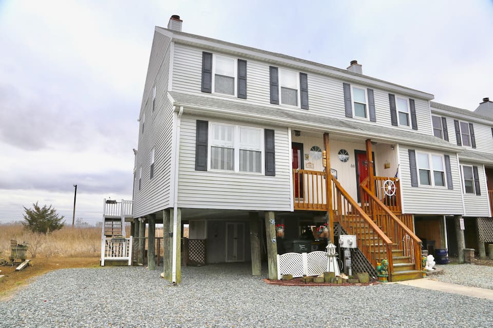 Charming gray townhouse with black shutters, and brown wooden staircase leading up to red front door.