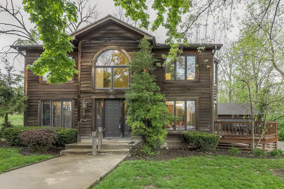 Gorgeous two story brown wooden home with numerous glass windows, and a lovely front yard.
