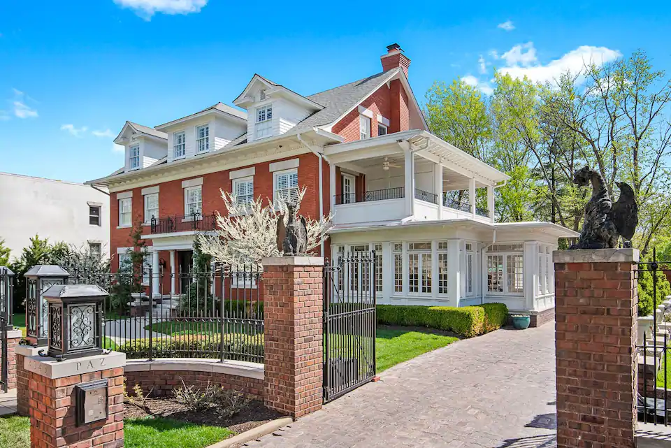 Photo of large red brick mansion with white sun room and wrought iron gate.
