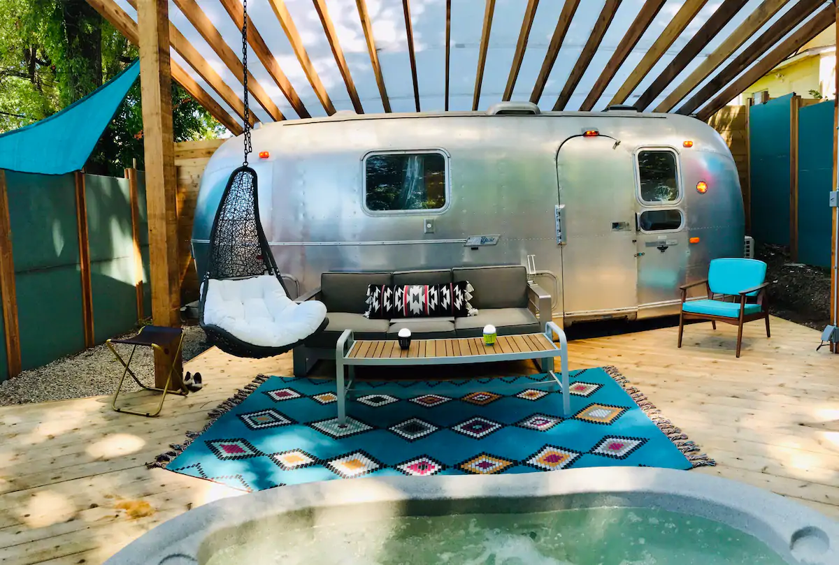 Shiny silver Airstream Trailer with plastic/wood over top and turquoise fencing, all for privacy with matching rug.