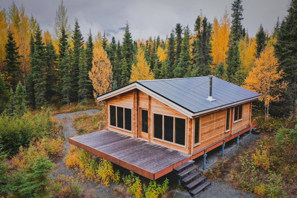 Beautiful Alaska cabin rental with lots of windows, green metal roof, large front deck and surrounded by autumn trees.