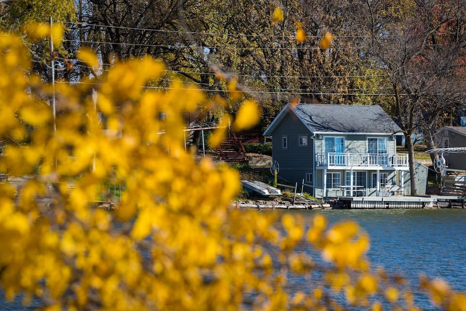 Blue cabin off in distance located right on lake with yellow leaves in foreground