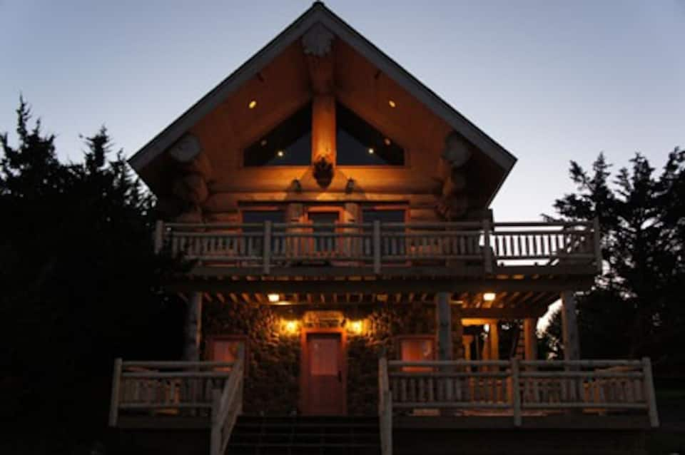 Twilight photo of beautiful cabin illuminated with soft white lights, with 2 balconies.