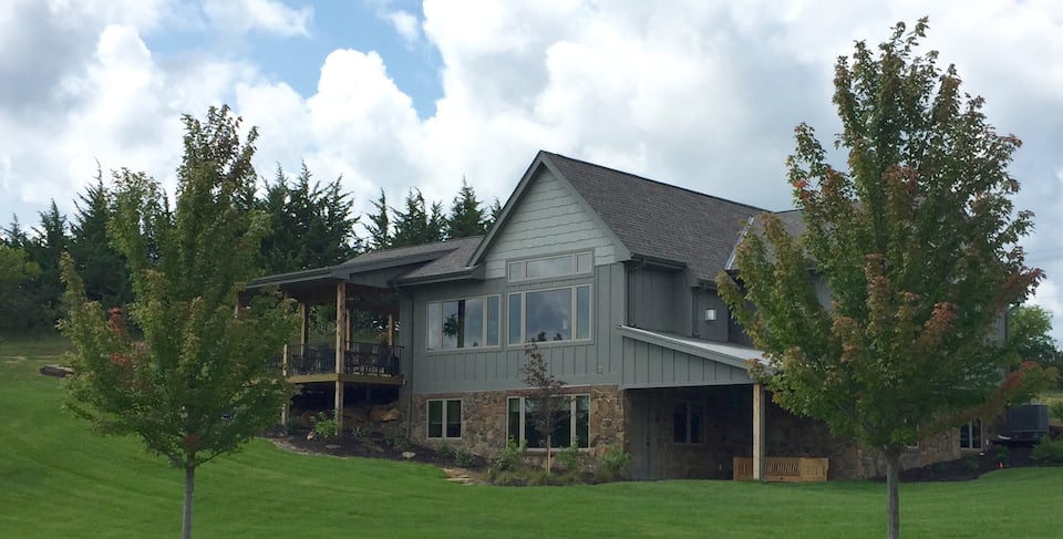 Large cabin with exterior stonework surrounded by lush green trees.