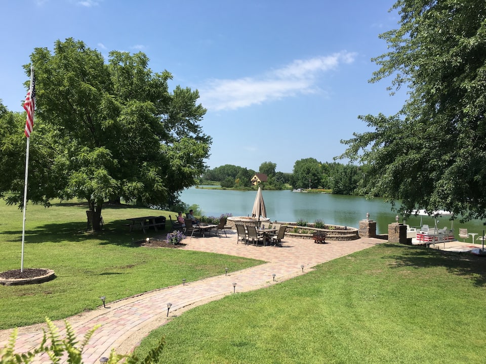 Stunning view of lake with upscale yellow brick patio and nice patio furniture. Lush green yard with brick walkway in the foreground. One of the best cabins in Nebraska.