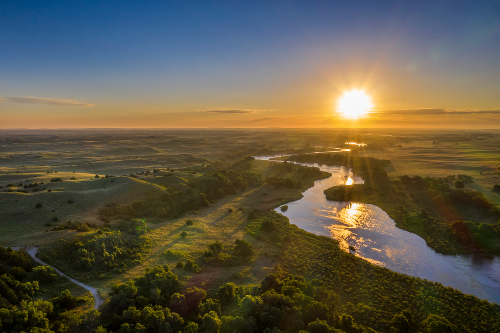 Photo of river meandering though Nebraska sandhills with sun setting in background.