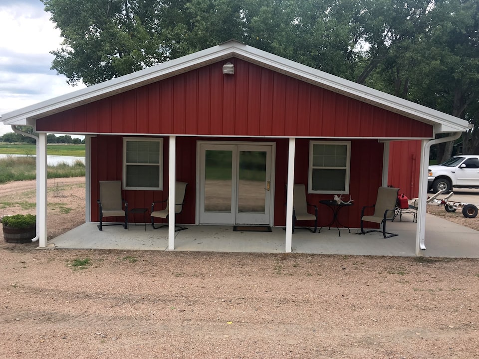 Red sided cabin, with double entry doors, and large patio with beige patio chairs.