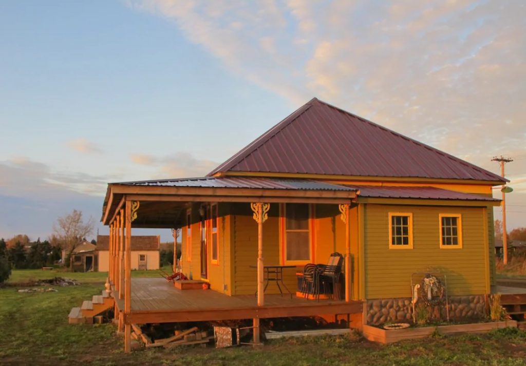 A charming 1915-era Folk Victorian cottage painted an olive green with a large porch that overlooks the Cannonball River at sunset