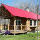 Log cabin with red rood and large front porch.