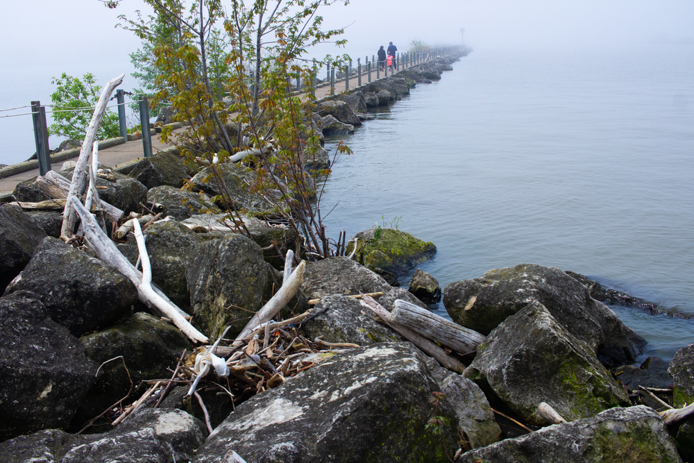 A long pier on Lake Erie with fog towards the end of it and rocks around it