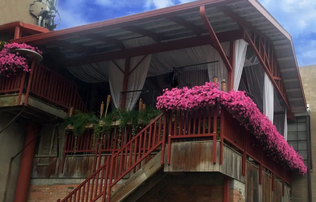 A large deck with a white wooden roof, white curtains, tiki torches, and pink flowers on the railing airbnbs in North Dakota
