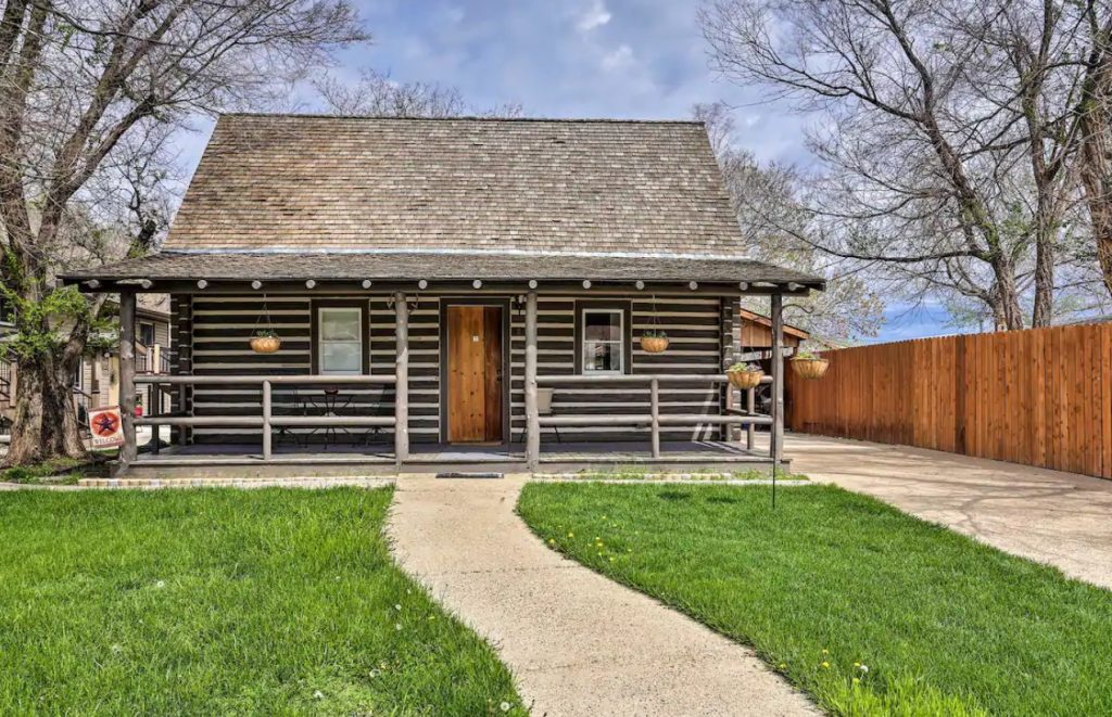 The exterior of a classic log cabin with a long fence next to it and a large green front yard