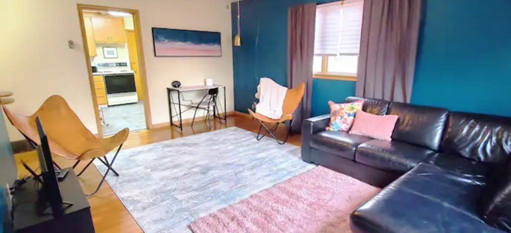 A large living room with a sectional sofa, two butterfly chairs, and teal and pink accents.