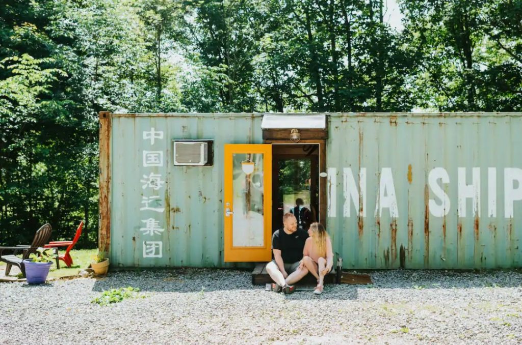 A couple sitting on the front stoop outside of a shipping container turned tiny home glamping in ohio
