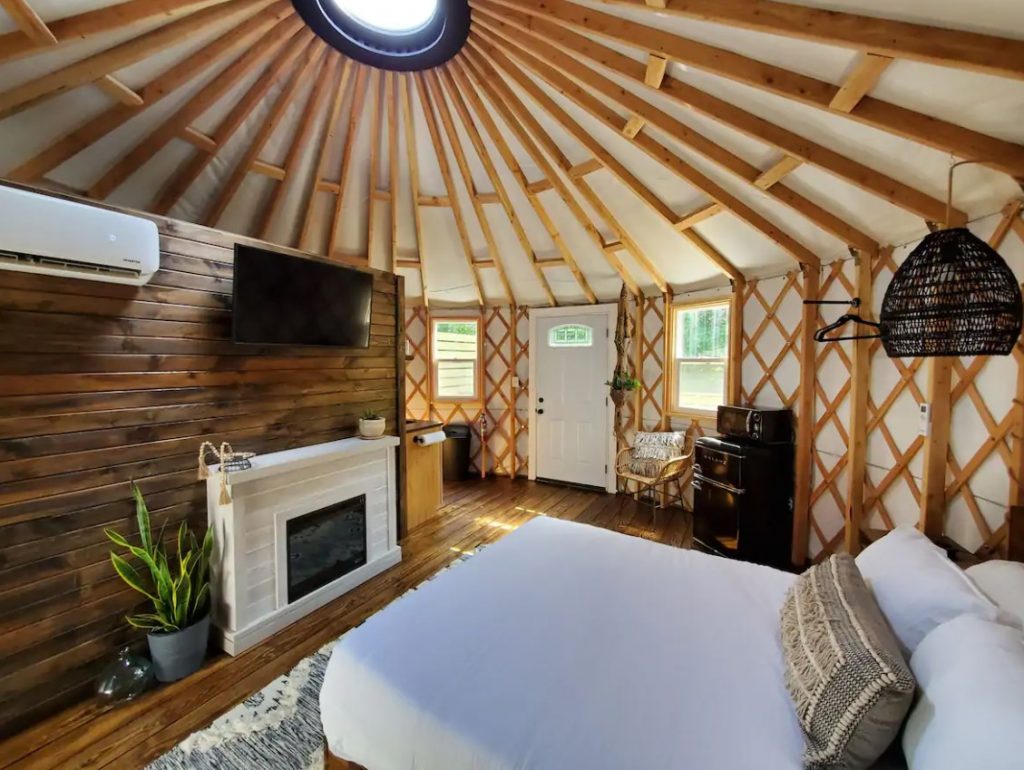 The inside of a luxury yurt in ohio with hardwood floors, a gas fireplace, and a queen sized bed.