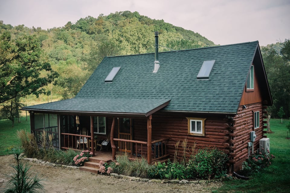 Rustic log cabin with cozy front porch and green roof.