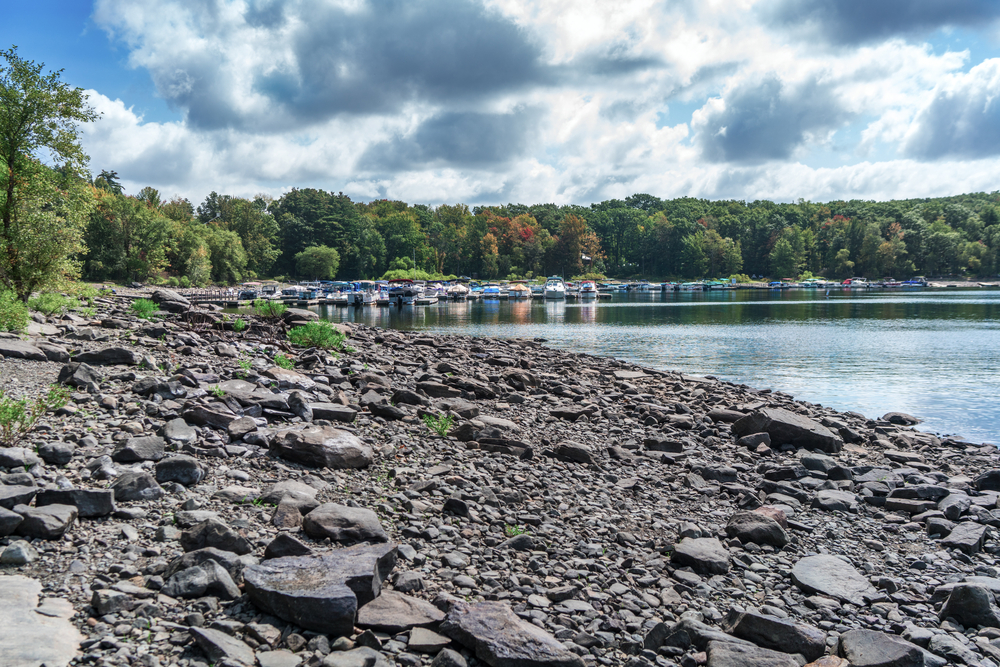 Rocky beach shore of Lake Wallenpaupack in small town Pennsylvania. Blue lake waters and marina in background.