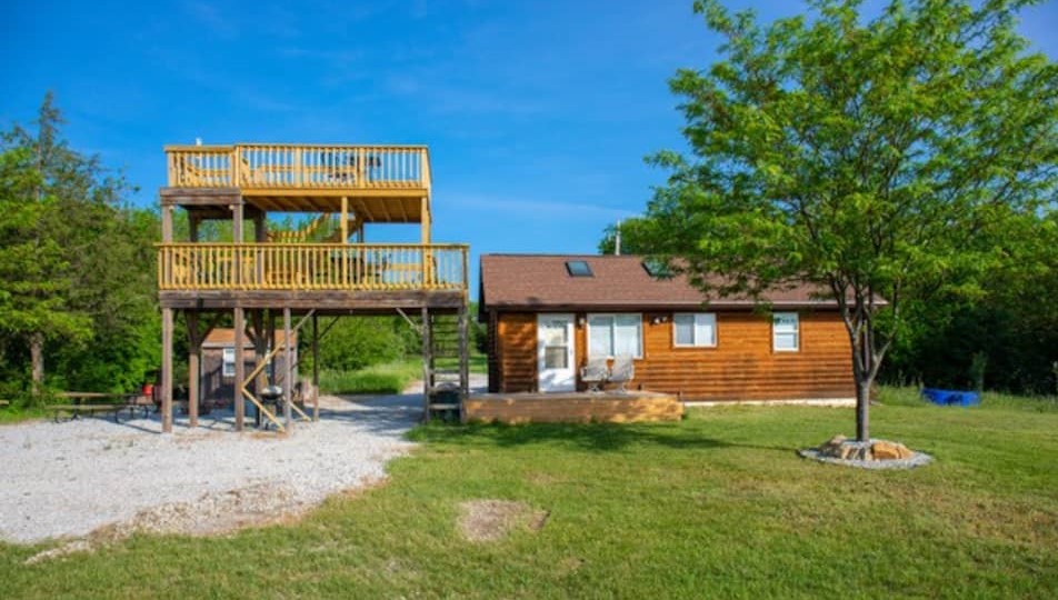 A small log cabin with a large two tier observation deck next to it surrounded by grass and trees Airbnbs in Nebraska