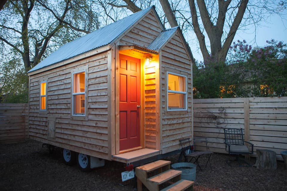 A small tiny home cabin with natural wood detailing outside, a red door, and plenty of windows Airbnbs in Nebraska