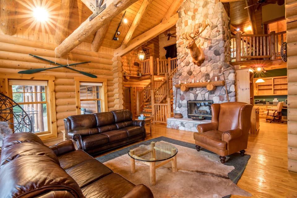 The inside of a luxury log cabin with leather couches, wood floors, wood walls, and a large stone fireplace.
