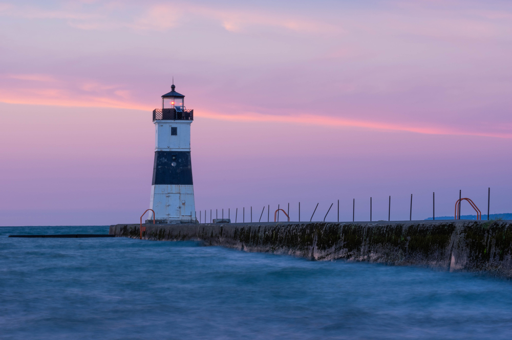 Lighthouse on Great Lakes in Erie as small town in PA. Pink sunset illuminates sky in background.