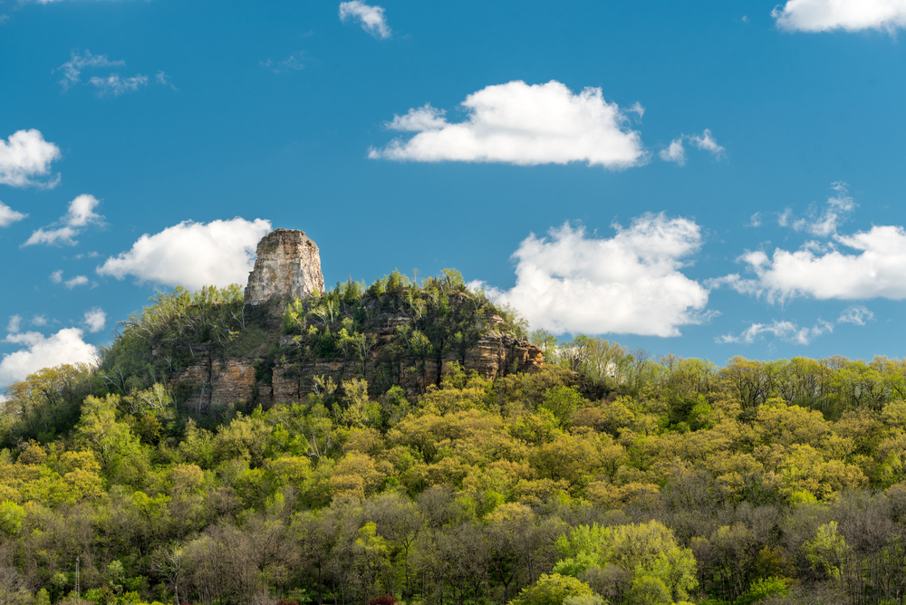 A bluff in the middle of summer surrounded by trees with a beautiful blue sky in Winona Minnesota