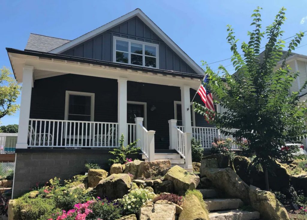 The exterior of a newly built VRBO in Ohio, a brown-sided cottage with white trim and steps leading down with rocky landscaping on either side.
