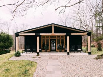 a large black cabin with a large covered front porch with natural wood columns. It is one of the best cabins in Hocking Hills.